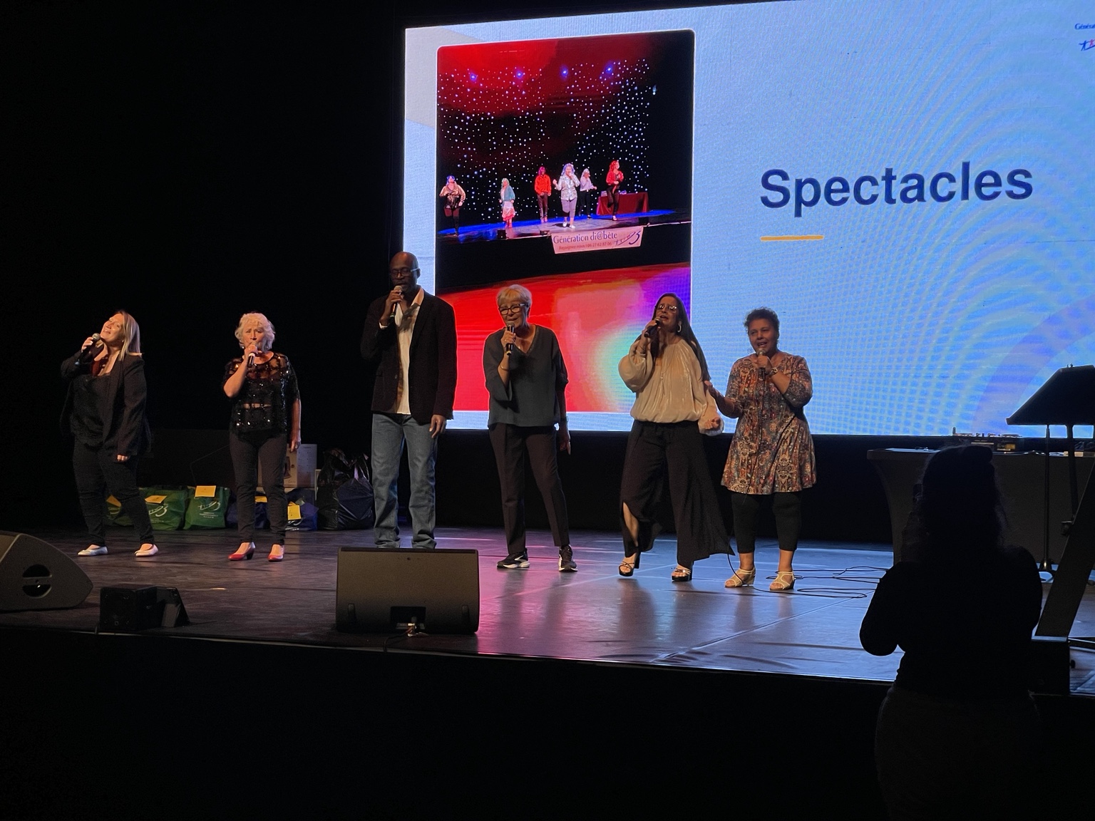 Six personnes chantent ensemble sur scène.