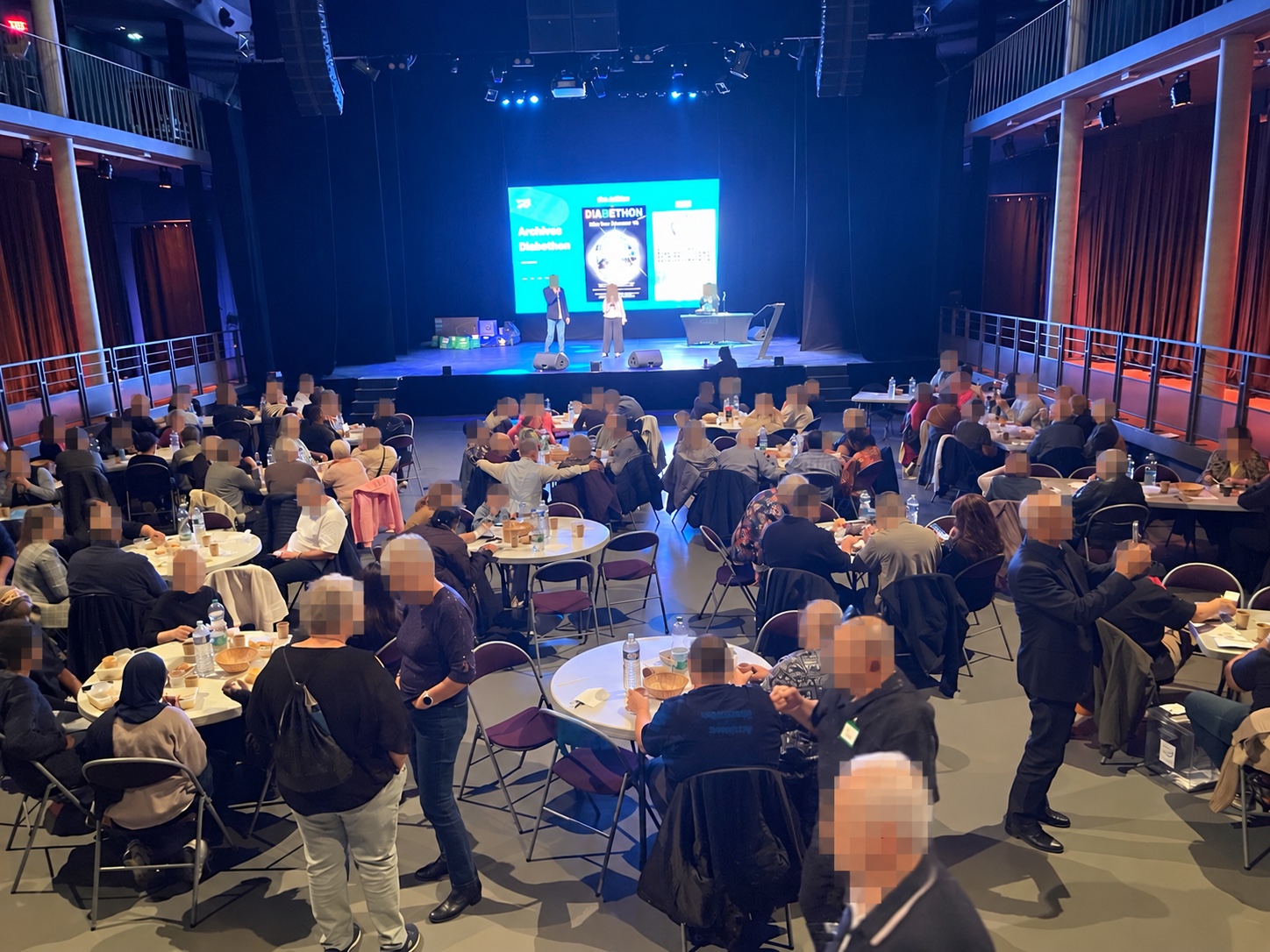 Vue d’ensemble du public et de la scène. Des visages sont masqués.