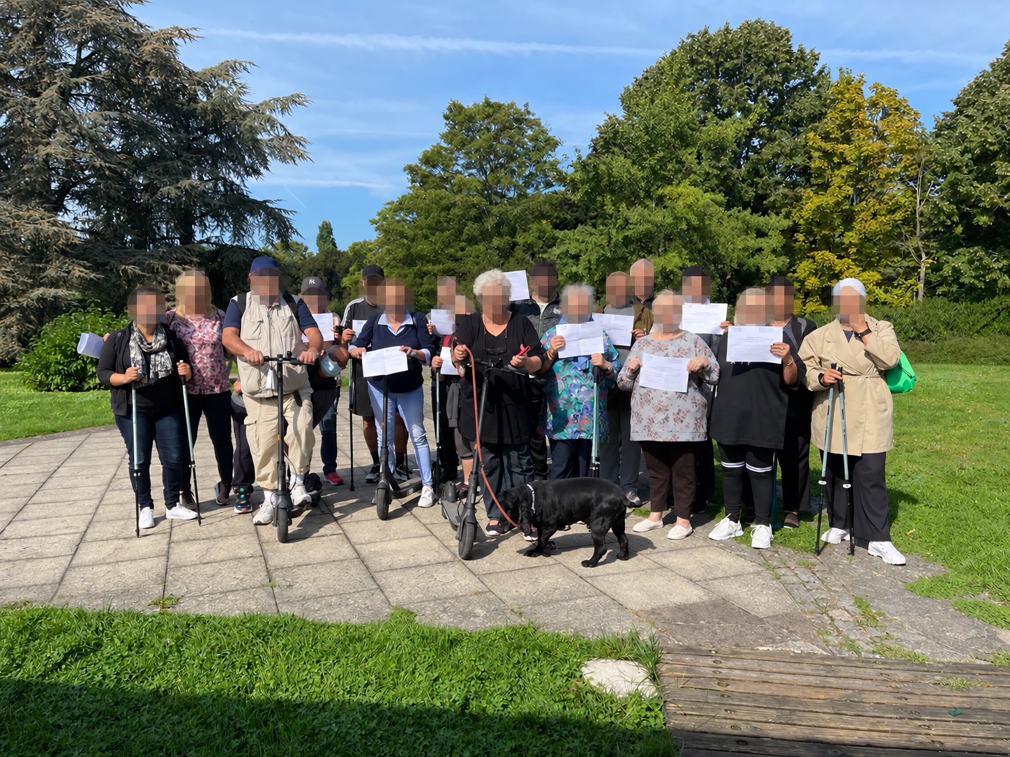 Un groupe réuni en plein air avec des bâtons de marche et un chien, les visages floutés.